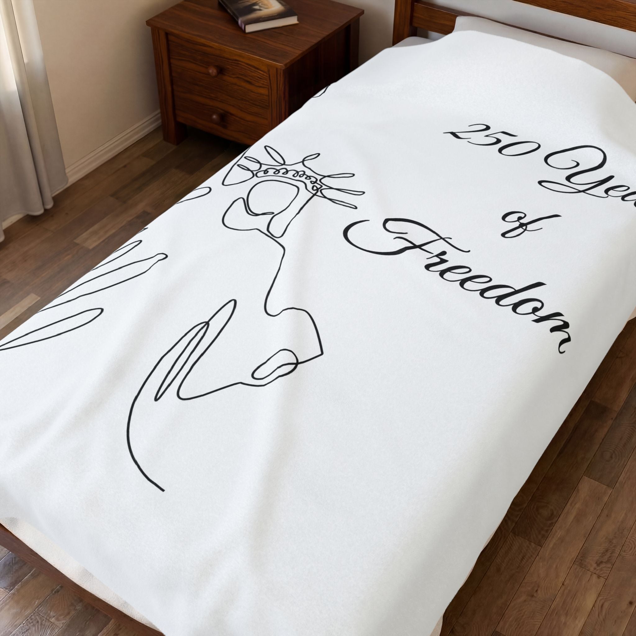 A white bedspread or blanket featuring a black continuous line drawing of the Statue of Liberty and the text '250 Years of Freedom', shown on a bed in a bedroom setting.