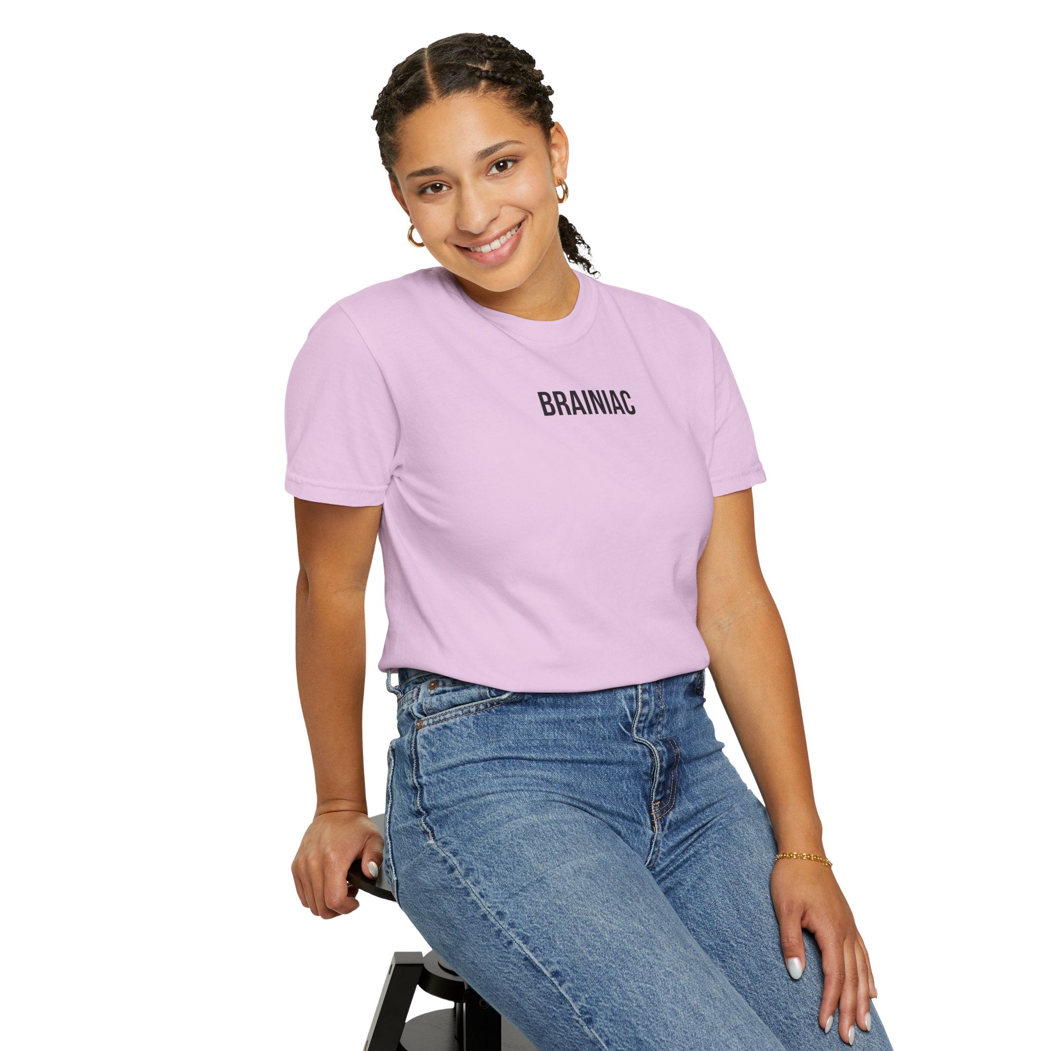 Person wearing a light purple t-shirt with 'BRAINIAC' text and blue jeans, sitting on a stool against a white background.