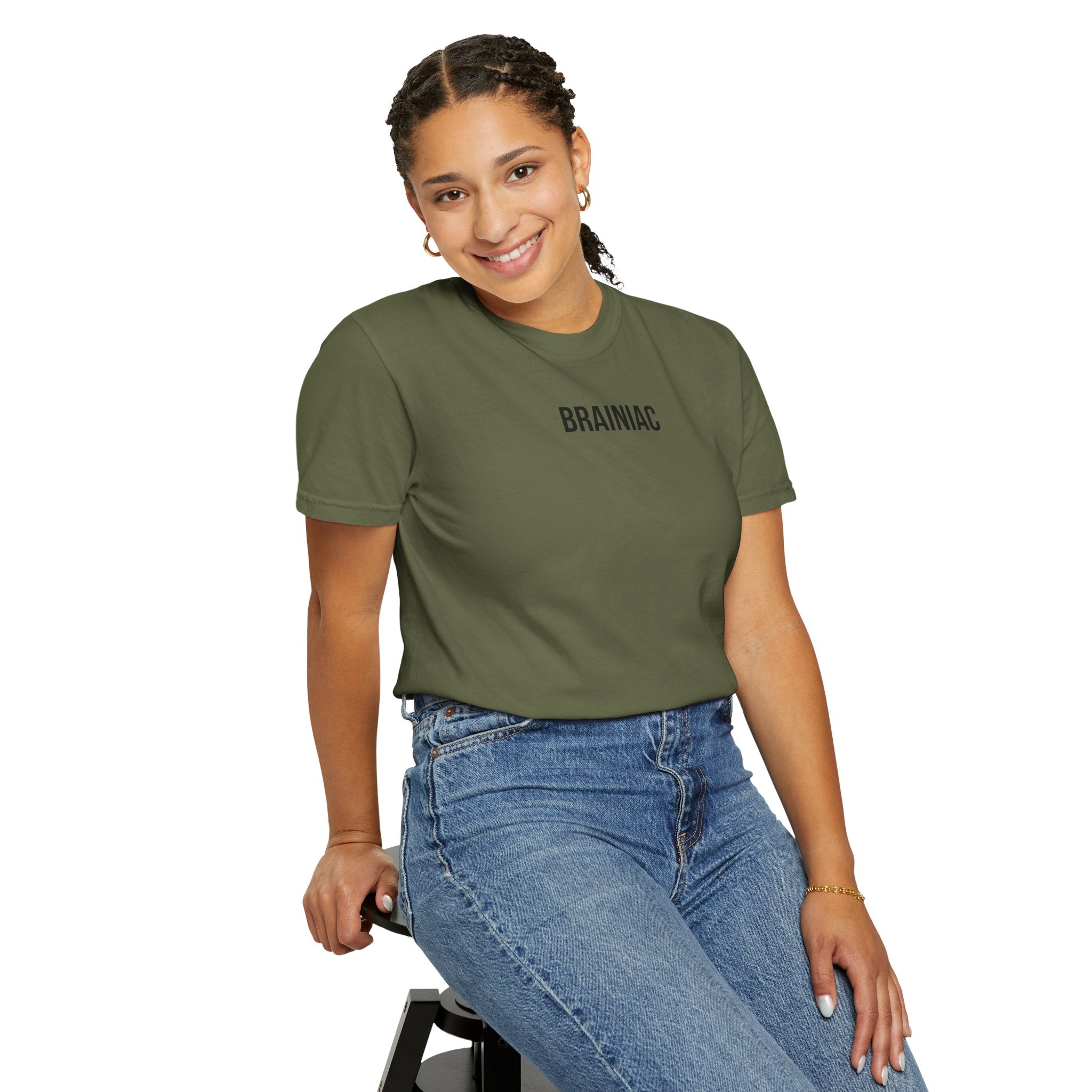 Woman smiling wearing a green t-shirt with 'BRAINiac' text and blue jeans, sitting on a stool against a white background.