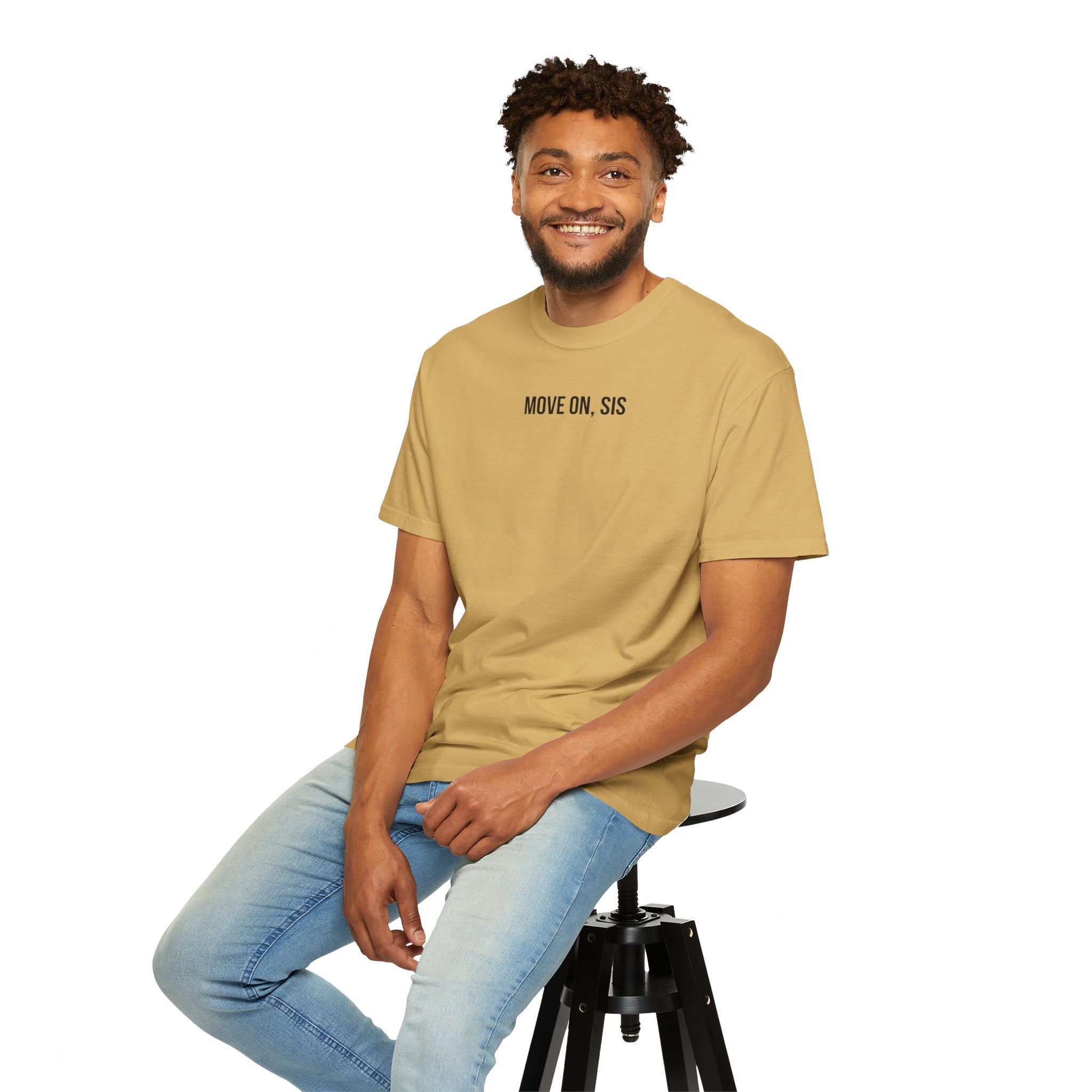 Man sitting on a stool wearing a gold t-shirt with text and light blue jeans on a white background